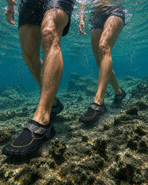 Personas caminando bajo el agua con zapatos acuáticos Manta Flow Black de uzi sport guadalajara sobre rocas marinas