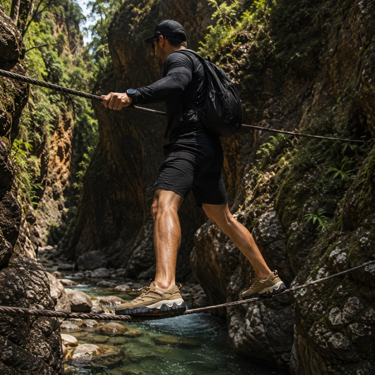 Hombre con zapatos uzi sport guadalajara Nómada color arena cruzando un río sobre cuerdas en un cañón natural.