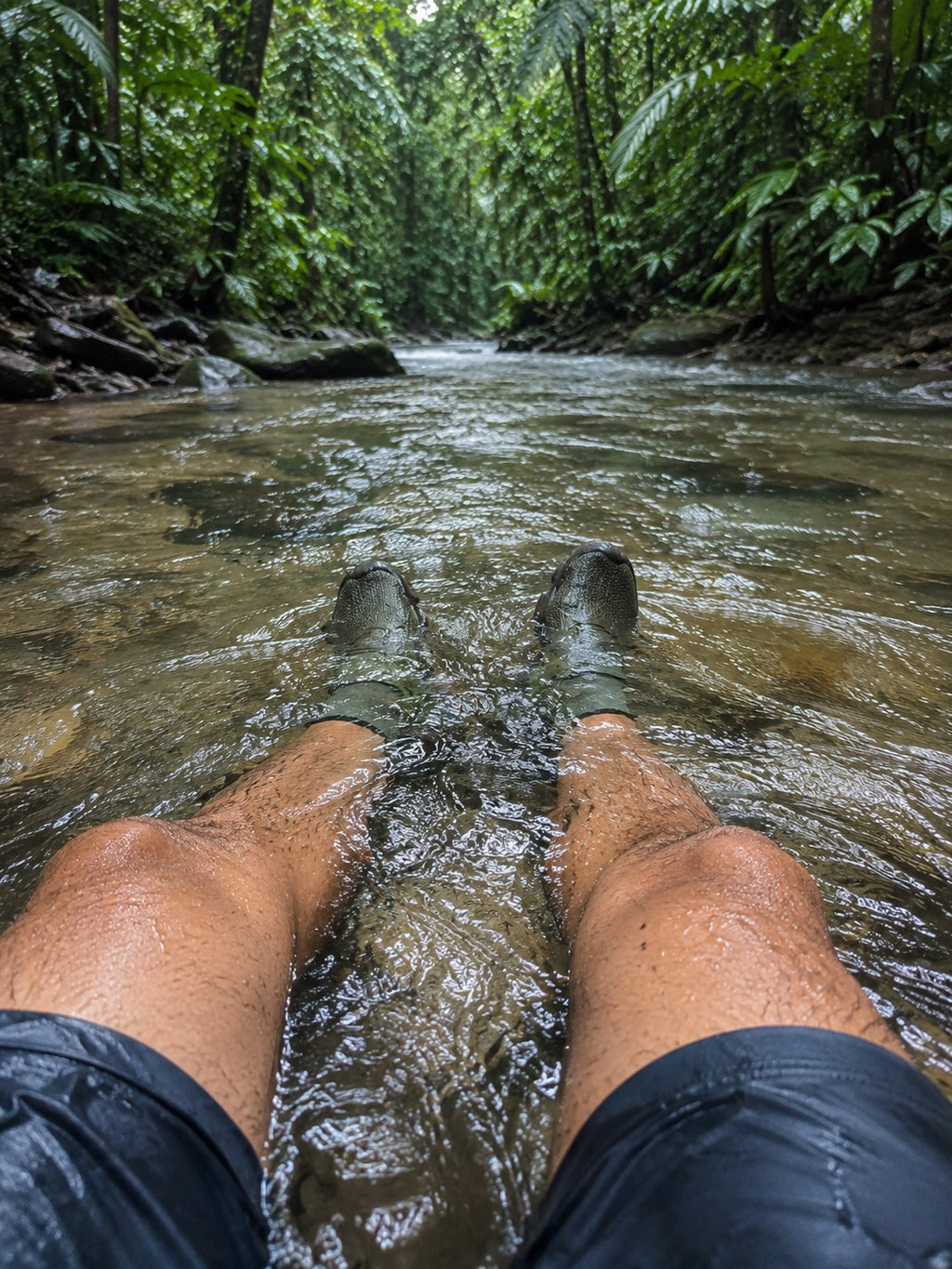 Persona usando zapatos sumergibles TrailWave de uzi sport guadalajara en un río rodeado de vegetación selvática.