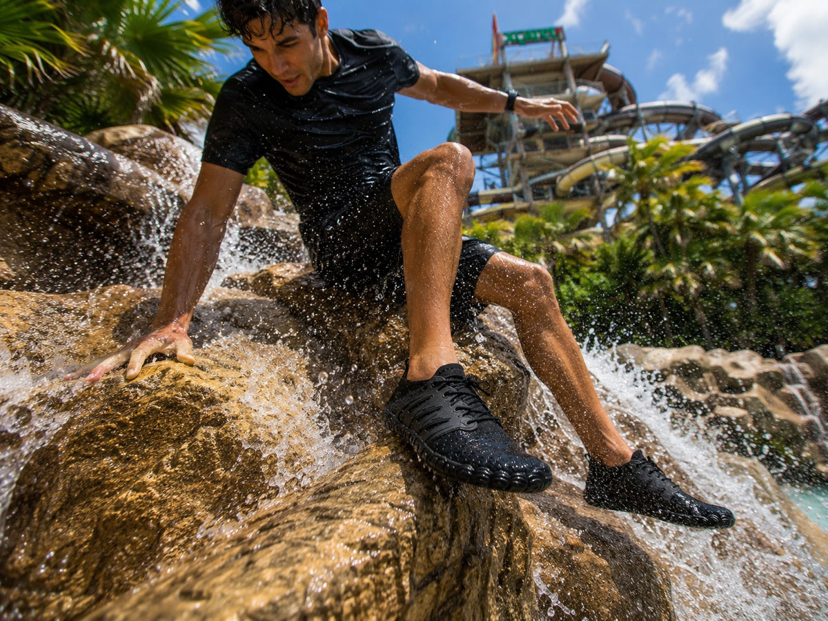 Hombre usando zapatos acuáticos negros uzi sport guadalajara sobre rocas mojadas en un parque acuático